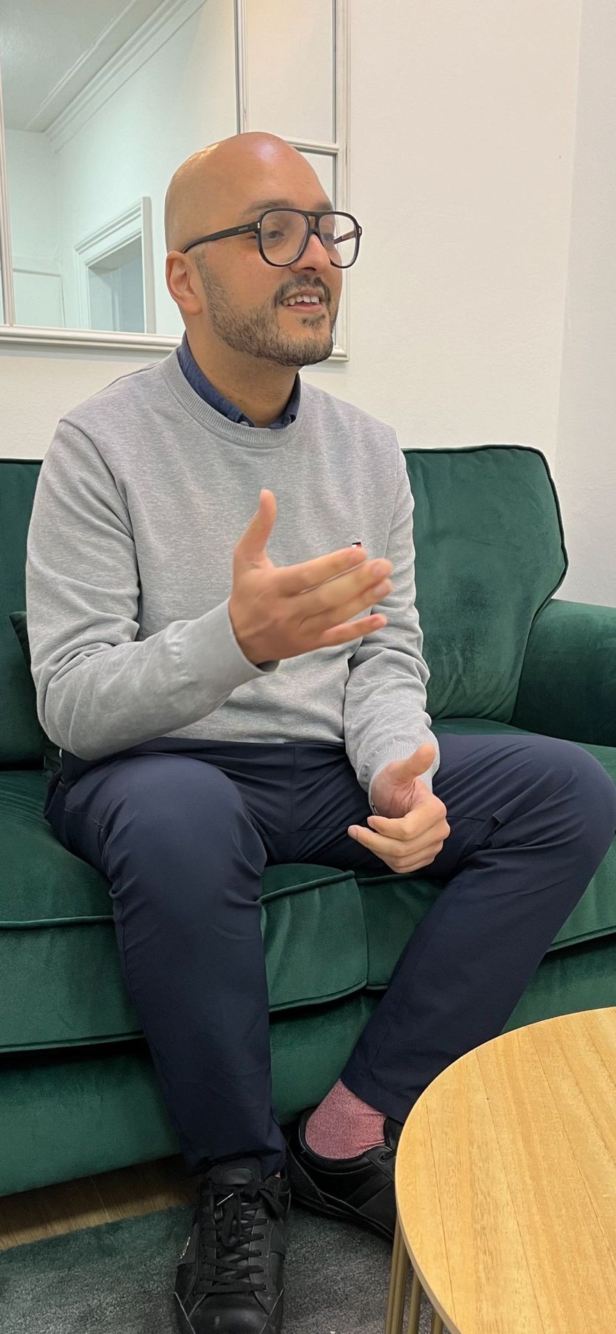 Person seated on a green couch, gesturing with one hand during a conversation.