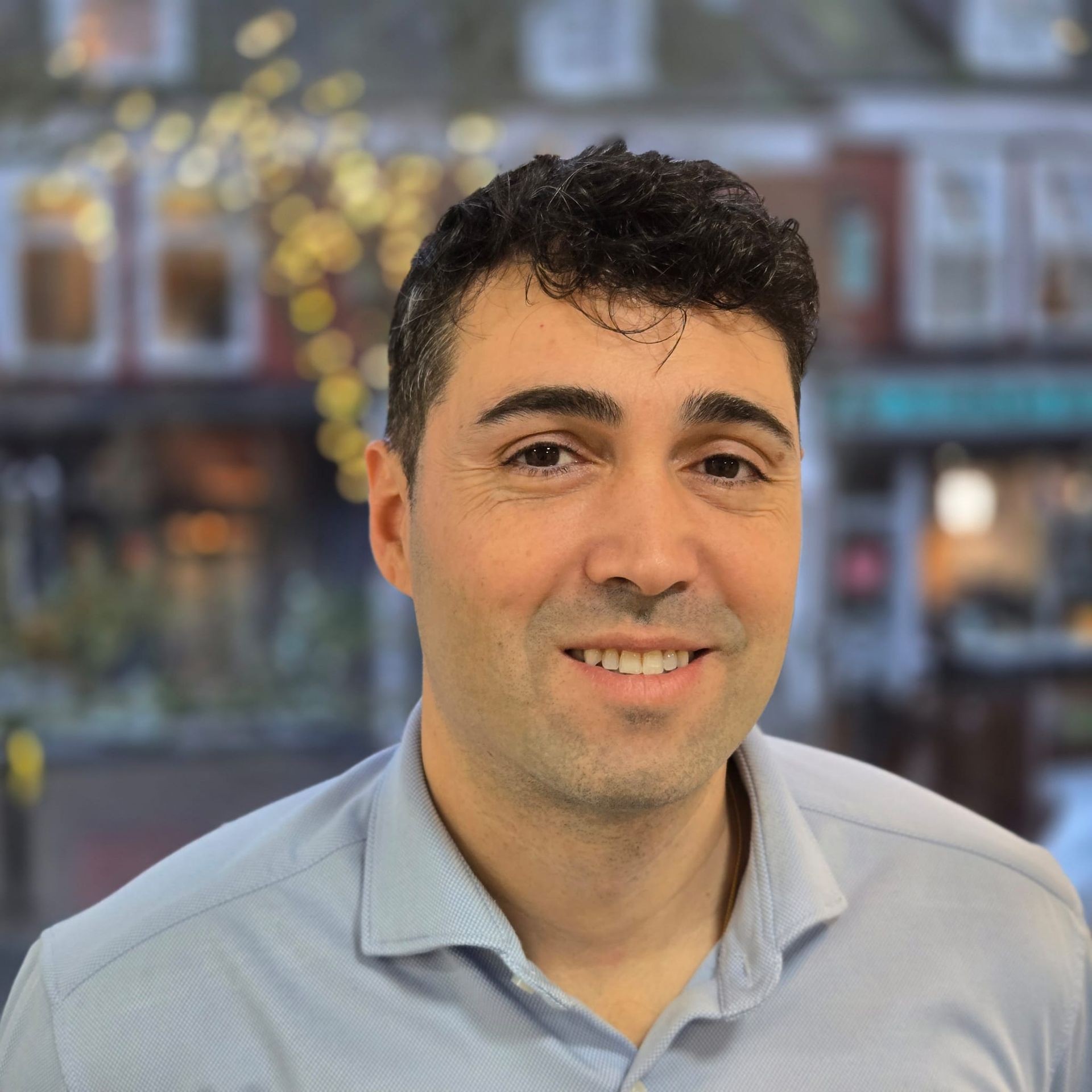 Person wearing a light blue shirt with a blurry background of buildings and lights.