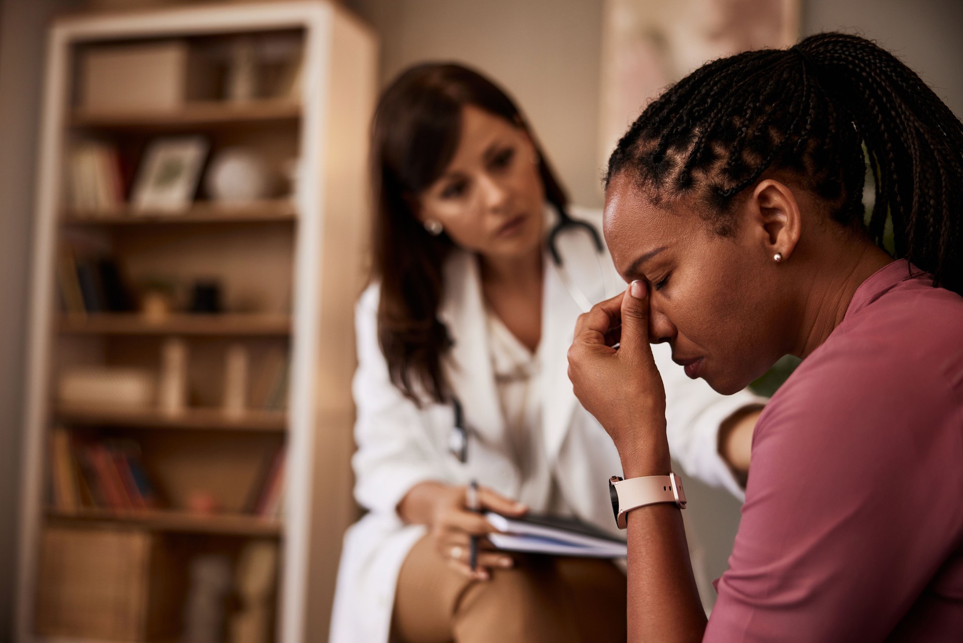 An African-American woman struggling with deep depression and talking with a female doctor.